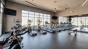 Une salle de sport équipée de tapis de course, de vélos elliptiques et de vélos d’appartement, disposés en rangées.