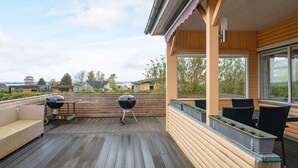 Una terraza de madera con dos parrillas de barbacoa, mobiliario exterior y vistas del vecindario.