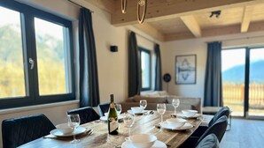 Uma sala de jantar com uma mesa de madeira posta para seis pessoas, seis copos de vinho e uma garrafa de vinho.