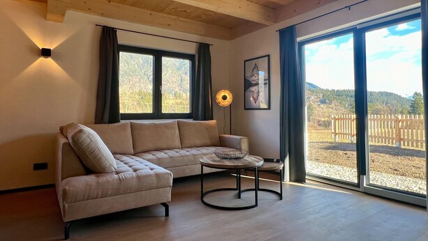 Uma sala de estar moderna com sofá seccional, mesa de centro redonda e grandes janelas com vista para o exterior.