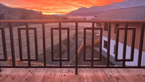 Um deck de madeira com guarda-corpo de metal, com vista para uma paisagem montanhosa ao pôr do sol.