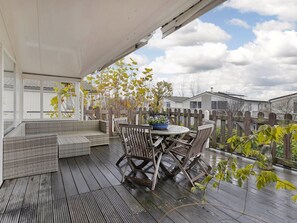 A covered patio with a wooden deck, wicker furniture, and a table with chairs. - Lovely Family Villa With Garden in Kamperland (Kamperland)