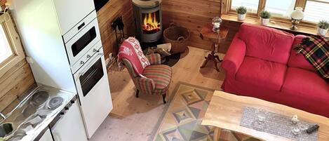 A cozy cabin interior with a wood-burning stove, a red sofa, and a kitchen area.