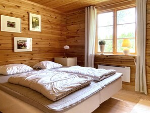 Quarto de cabana de madeira com cama, mesa de cabeceira, abajur e quadros na parede.