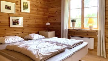 Un dormitorio de cabaña de madera con cama, mesita de noche, lámpara y ventana con cortinas.
