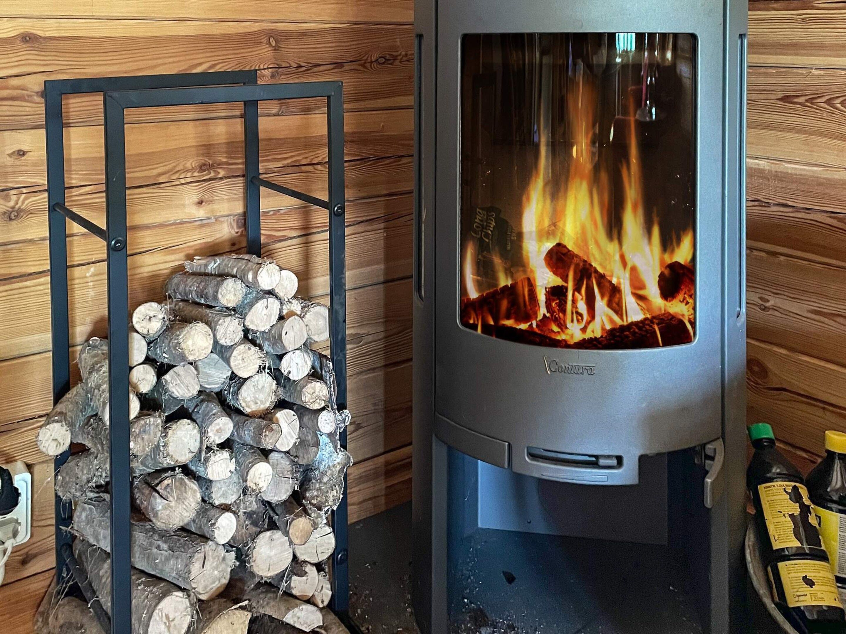En vedeldad kamin med ett metallställ för ved, placerad framför en vägg av trä.