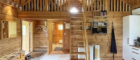 A wooden interior with a central staircase, wooden walls, and a kitchen area.