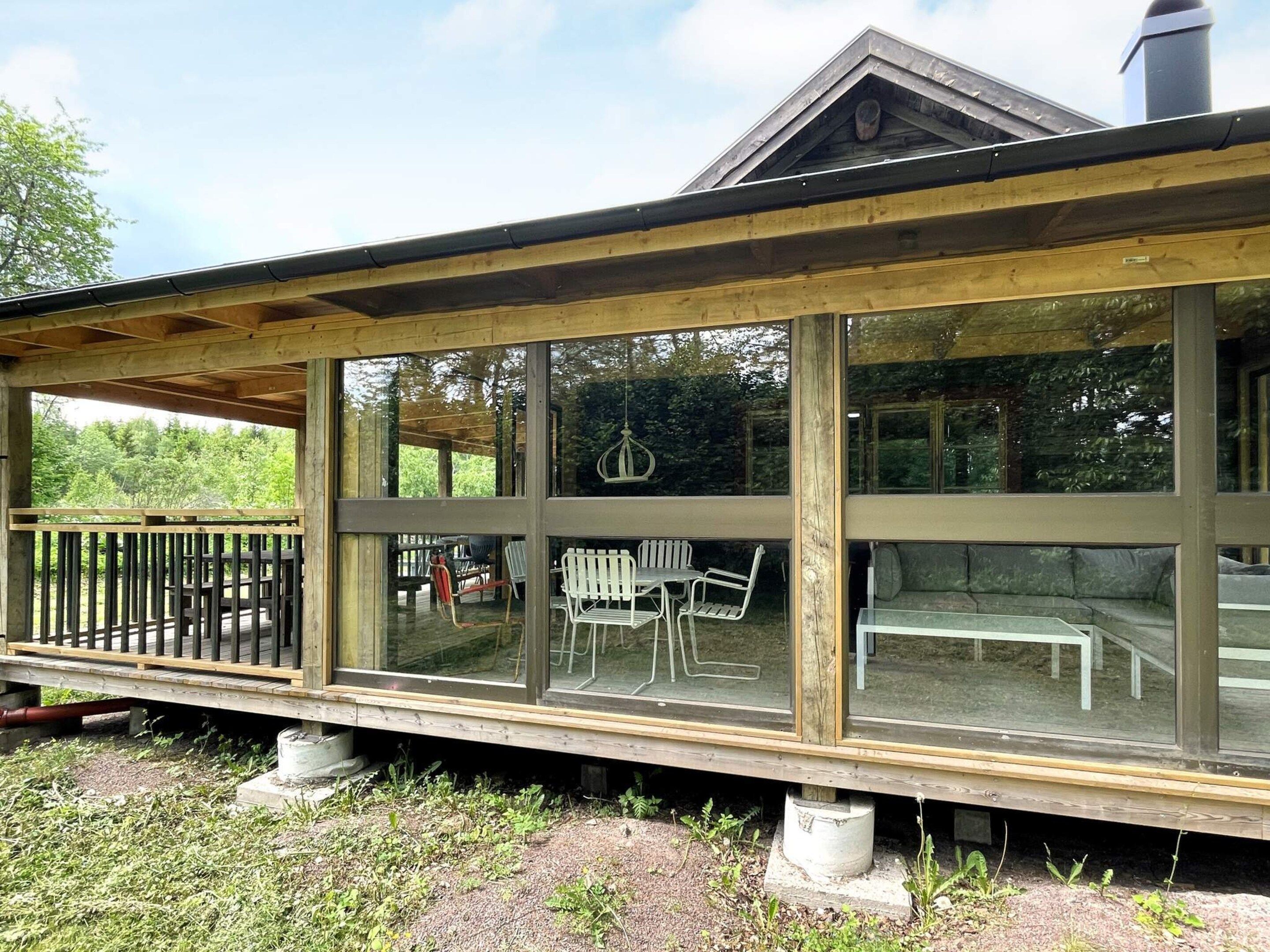 A covered outdoor area with a wooden deck, large windows, and outdoor furniture.