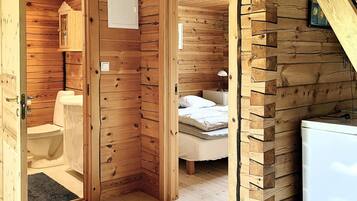 A wooden cabin interior with a bathroom, a bed, and a small kitchenette.