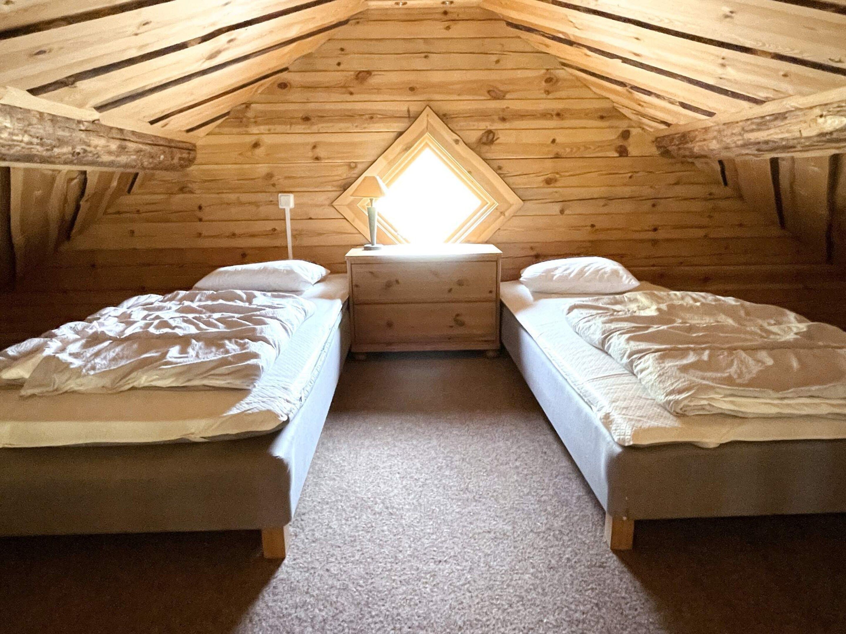 A small, cozy attic bedroom with two beds, a nightstand, and a window with a view.