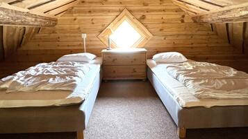 A small, cozy attic bedroom with two beds, a nightstand, and a window with a view.