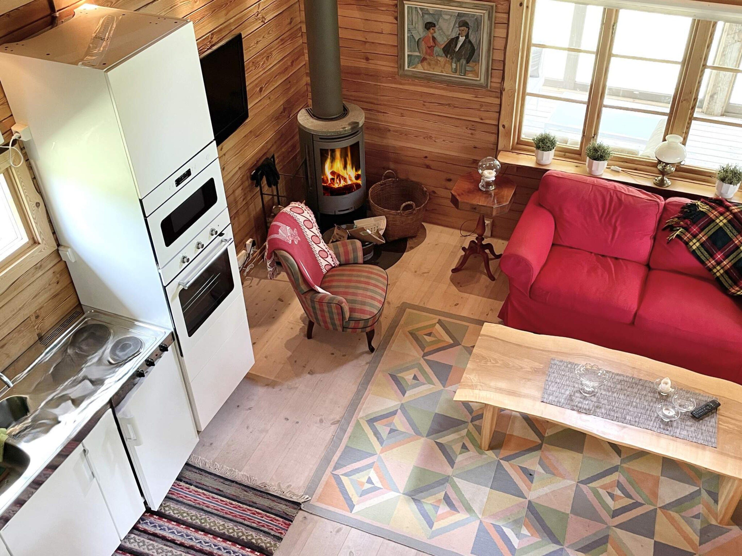 Een gezellig chaletinterieur met een houtkachel, een rode bank, een keuken met fornuis en een vloerkleed met dessin.