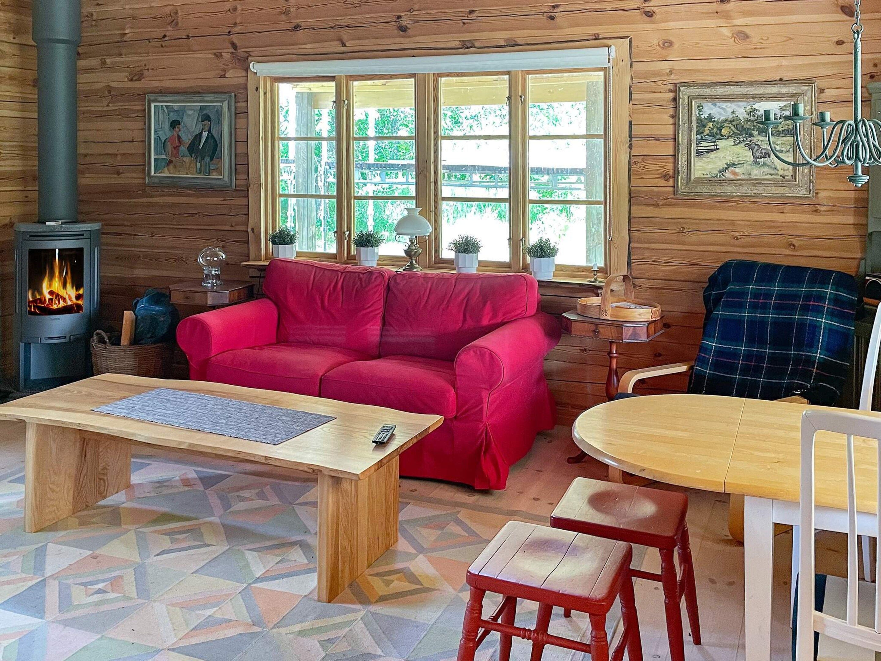 A cozy cabin interior with a red sofa, wooden dining table, and a fireplace.