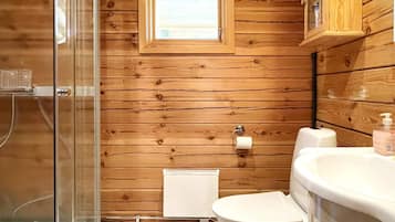 Un baño con paneles de madera, cabina de ducha de vidrio, inodoro y lavamanos.