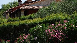 Un bâtiment en pierre, doté d’un toit en tuiles, entouré d’une végétation luxuriante et de plantes en fleurs.