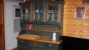 Un mueble de madera con puertas de cristal, un televisor sobre un pedestal de madera, y una mesita con un cuenco y una botella.