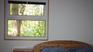 Un dormitorio con una cama de madera, una mesita de noche y dos ventanas con vistas a árboles.