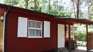 Una cabaña roja de madera con contraventanas blancas, un porche y un pequeño jardín.