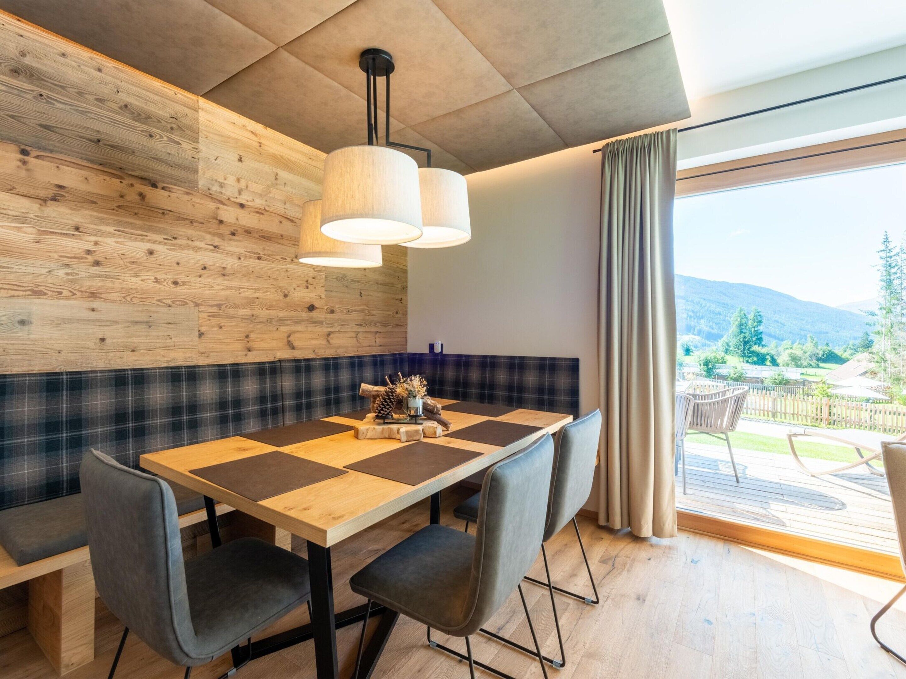 A dining area with a wooden table, grey upholstered chairs, and a plaid bench.
