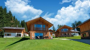 A cluster of wooden cabins with large windows and balconies, surrounded by lush green grass and trees under a clear blue sky. - Chalet in Wolting in a Delightful Area (Tamsweg)