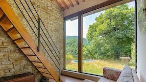 A room with a wooden staircase, a large window with a view of a swimming pool and greenery, and a floral sofa. - Villa in Borgo Pace With Private Pool (Borgo Pace)