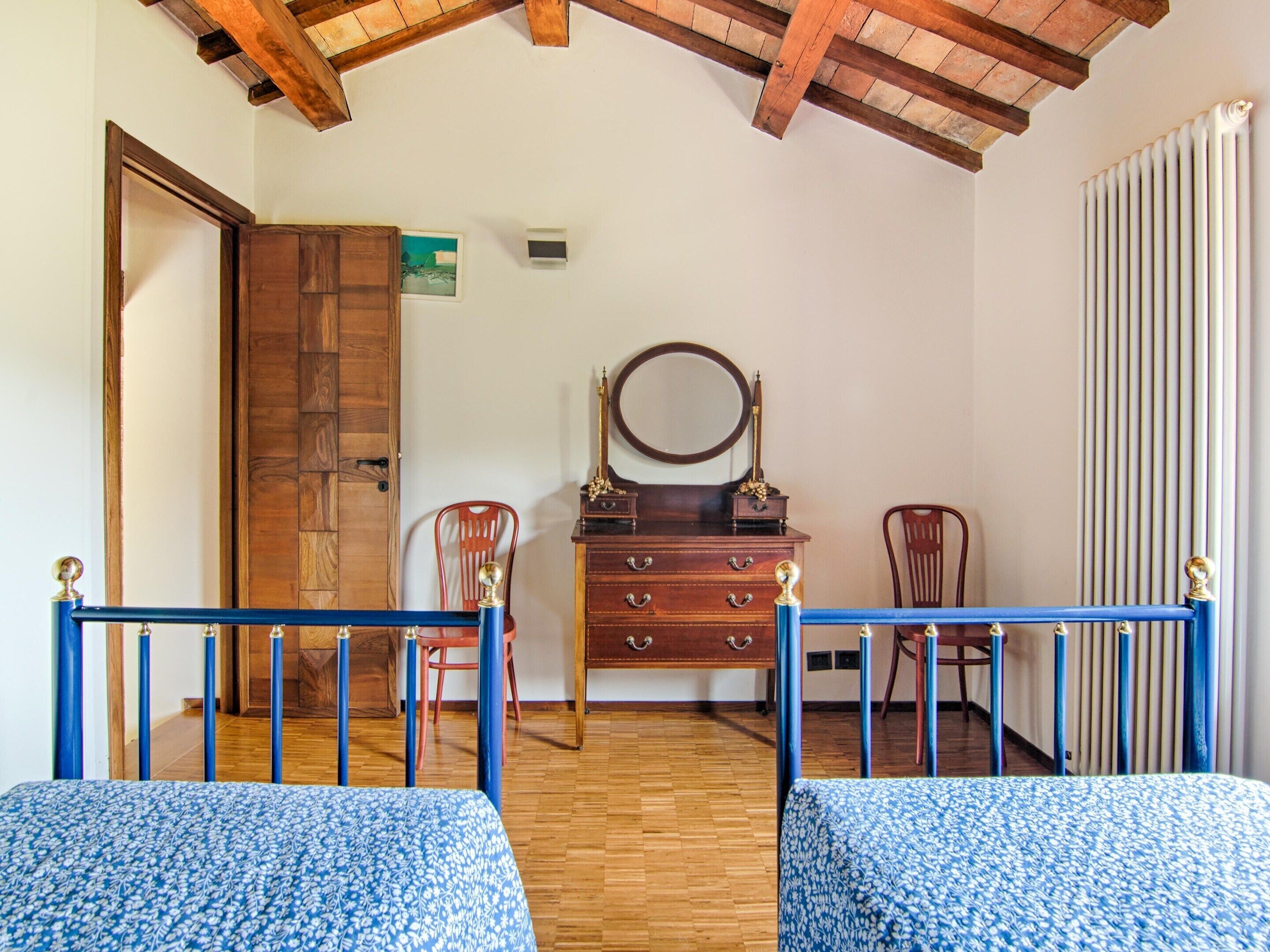 Une chambre avec deux lits, une commode en bois, un miroir et un radiateur.