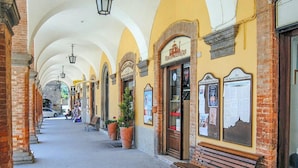 A covered pedestrian walkway with benches, potted plants, and storefronts. - Villa in Borgo Pace With Private Pool (Borgo Pace)