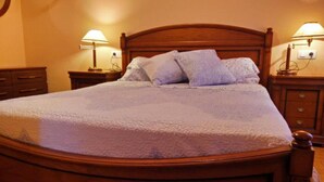 Una cama de madera con colcha blanca y dos almohadas, flanqueada por mesitas de noche con lámparas.