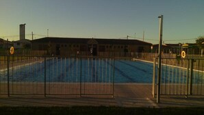 Una piscina con valla, un edificio al fondo y un cielo despejado.