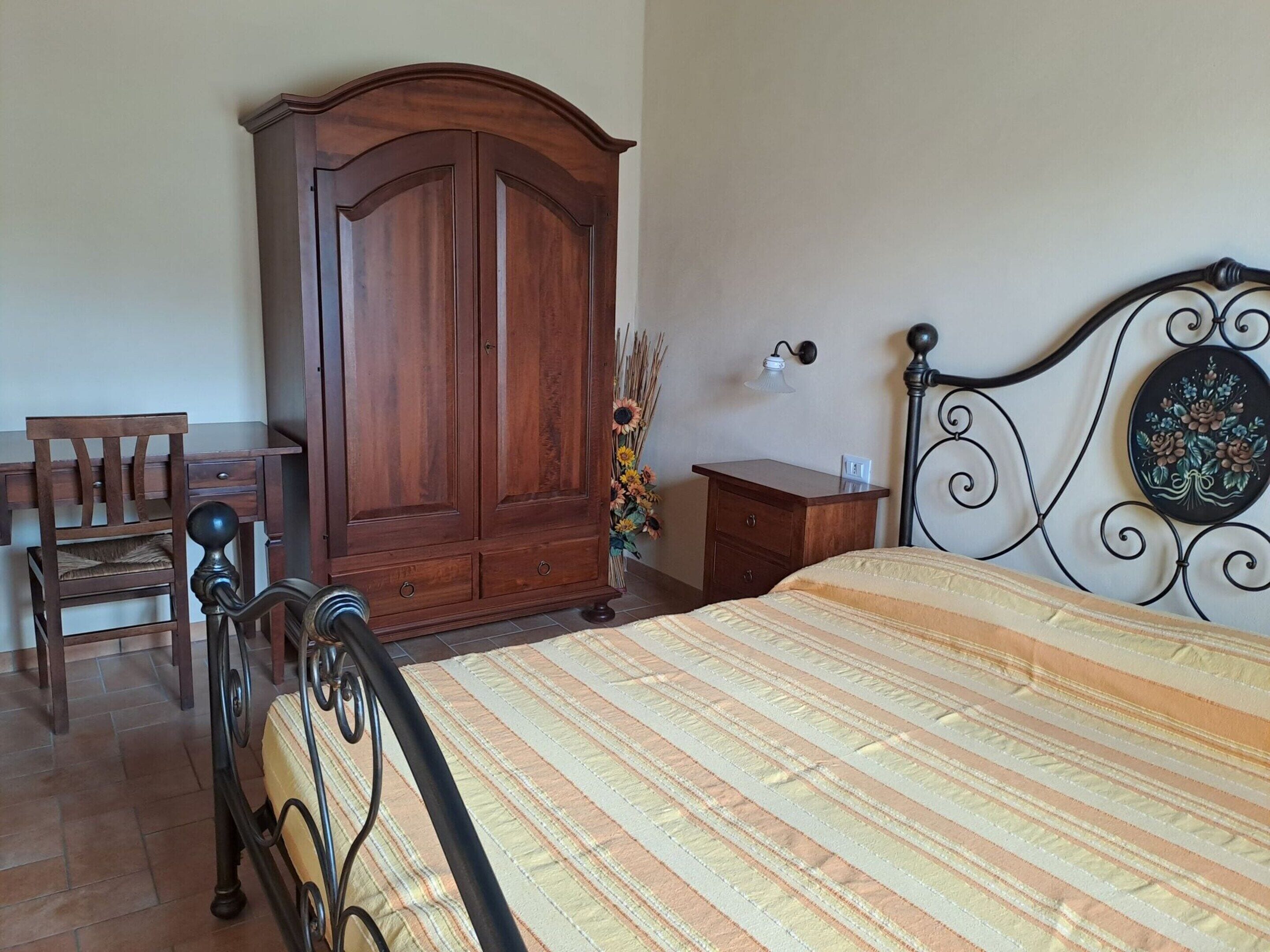 Une chambre à coucher comprenant un lit, une armoire en bois, un bureau avec une chaise et une table de chevet avec une lampe.