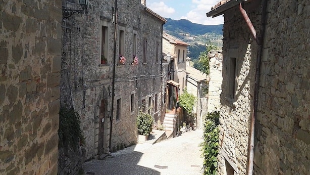 A narrow cobblestone street flanked by historic stone buildings with visible windows and doors, leading to a hillside. - Terrace Retreat in the Marche (Pennabilli)