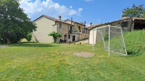 A grassy backyard with a stone house, a stone wall, and a soccer goal. - Terrace Retreat in the Marche (Pennabilli)
