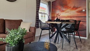 Ein modernes Wohnzimmer mit einer braunen Couch, einem Esstisch mit schwarzen Stühlen, einer Topfpflanze und einer Wanduhr.
