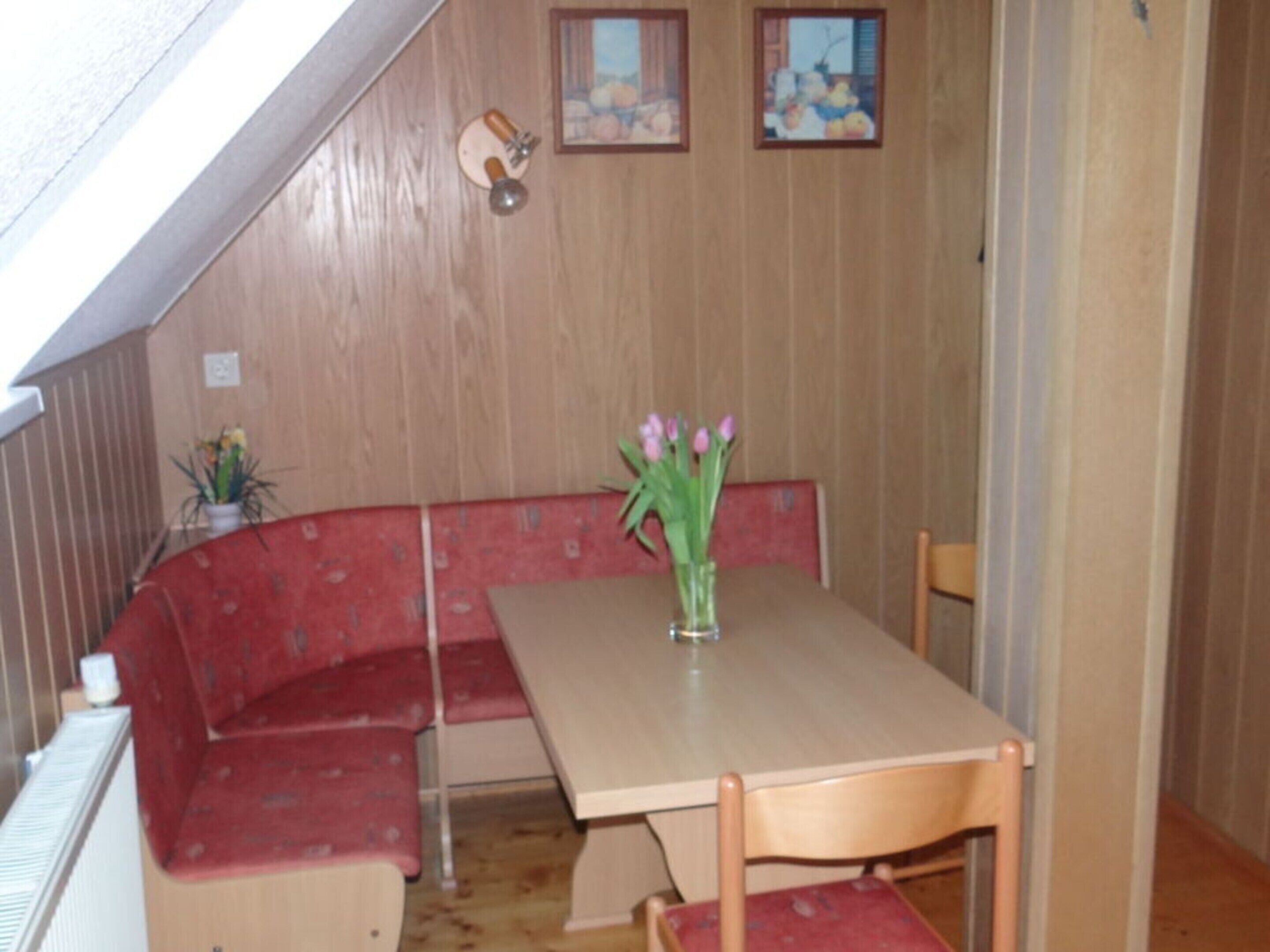 A dining area with a wooden table, red upholstered bench seating, and a vase with flowers.
