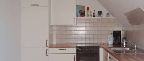 A compact kitchen with white cabinets, a built-in oven, a coffee maker, and a shelf with kitchen items.