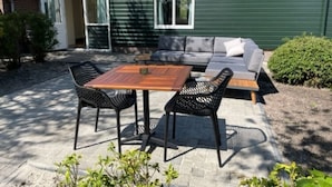 A patio with a wooden table and chairs, a sofa, and a sliding glass door leading to a room. - Holiday Home in Schoonloo With Balcony/terrace (Schoonloo)