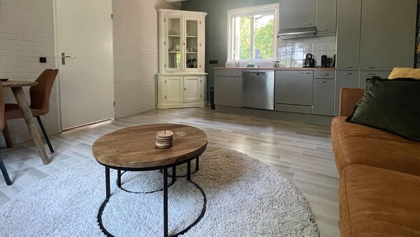 A modern kitchen with grey cabinets, a window, and a dining area with a round table and chairs. - Holiday Home in Schoonloo With Balcony/terrace (Schoonloo)