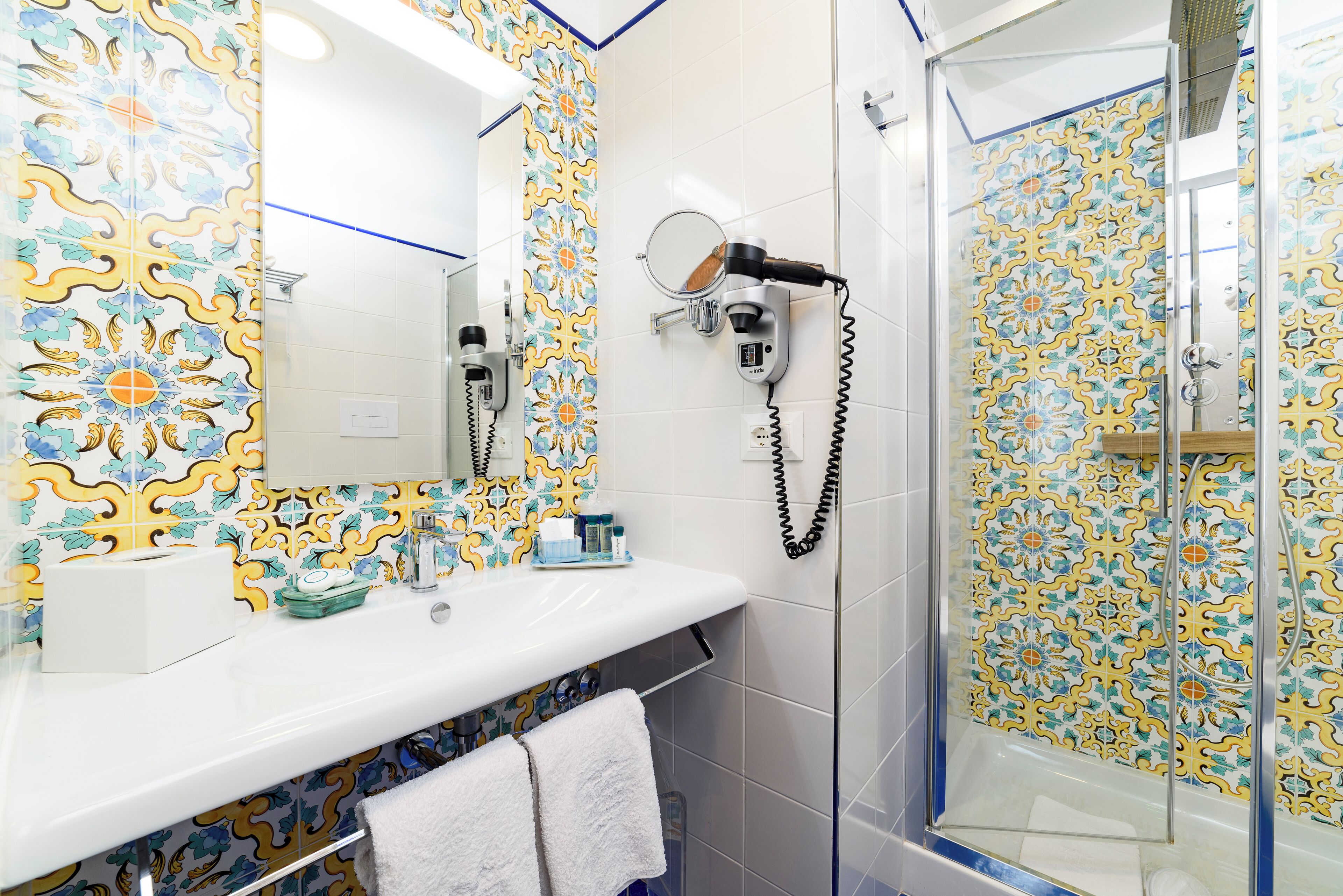 A bathroom with a white sink, a mirror, a hairdryer, and a shower with patterned tiles.