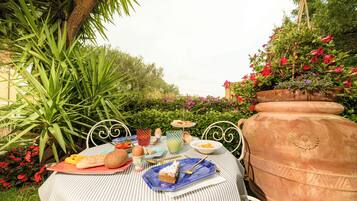 An outdoor dining area with a table set for a meal, surrounded by lush greenery and flowers.