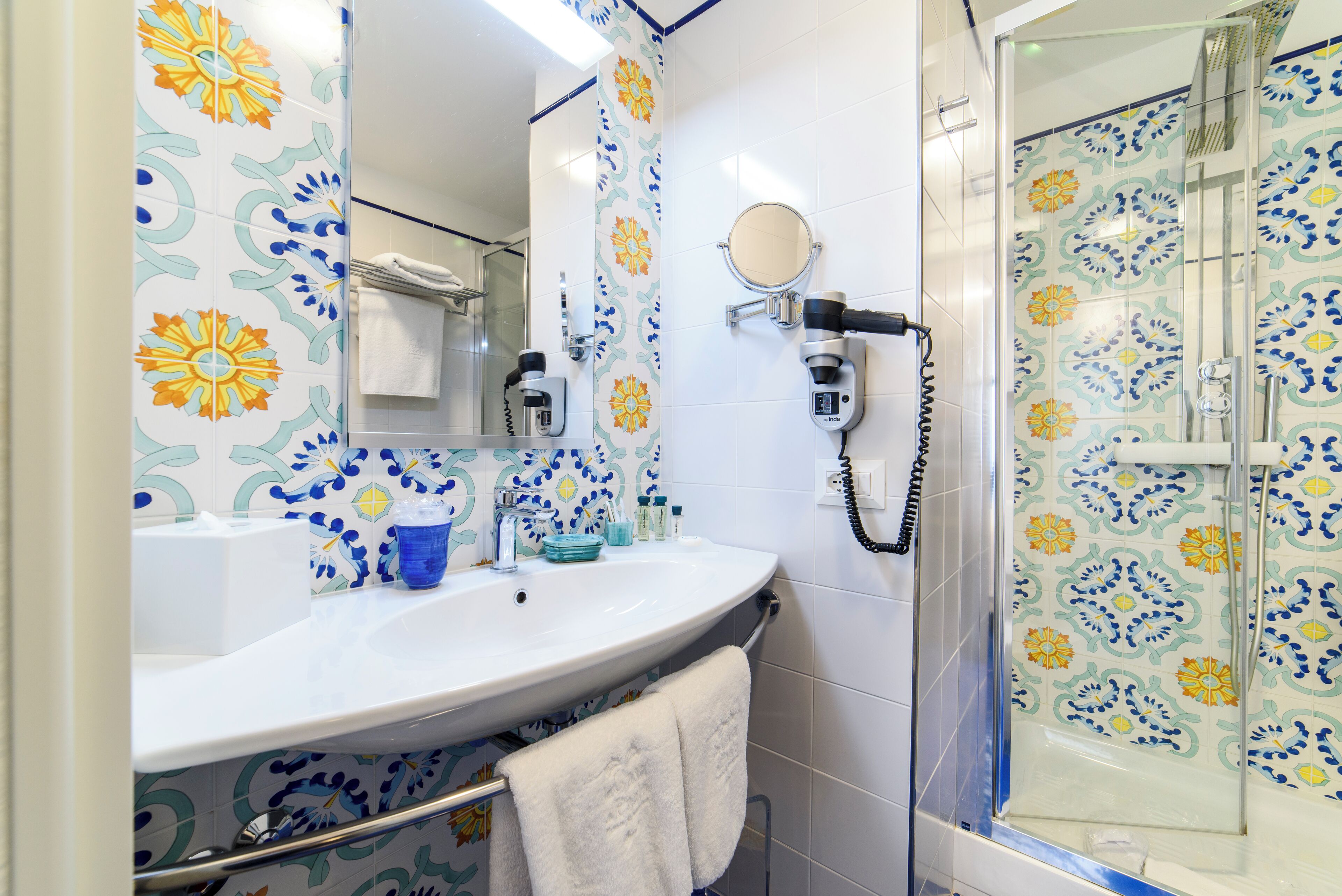 A bathroom with a white sink, a mirror, a towel rack, and a shower area with patterned tiles.