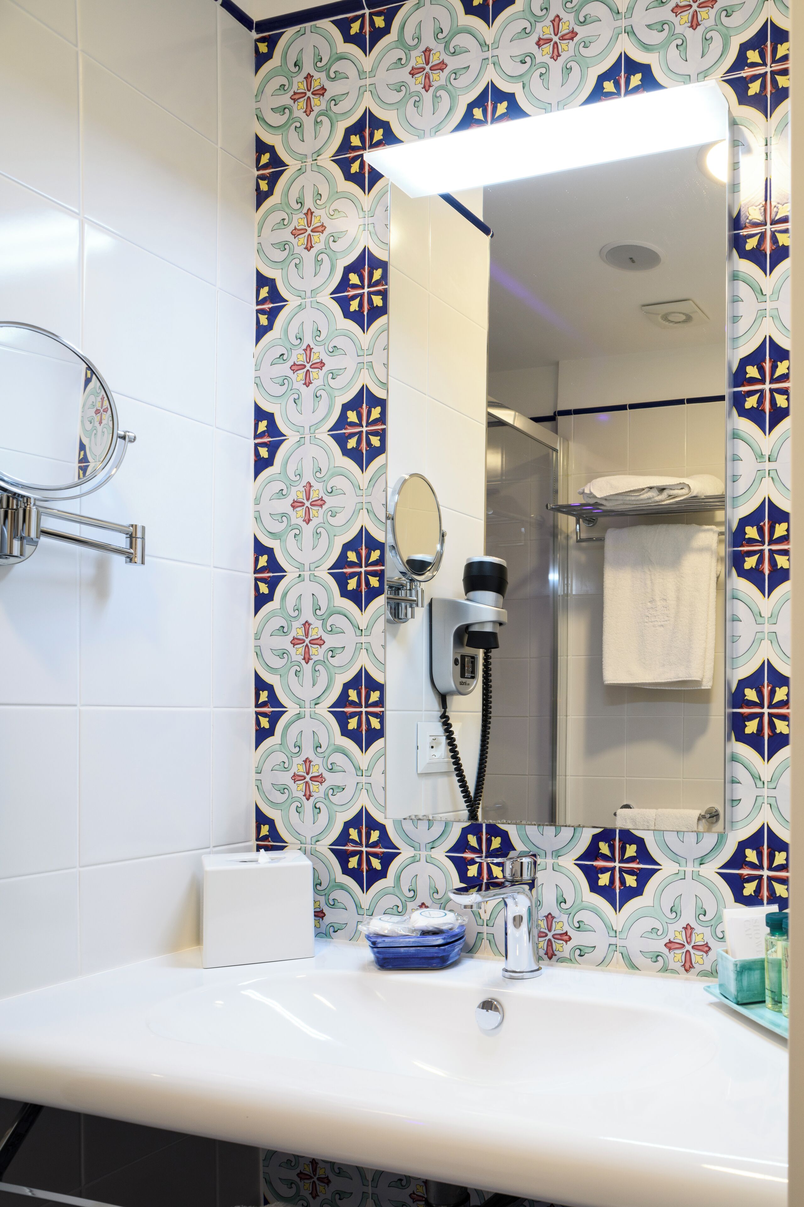 Un baño con lavamanos blanco, espejo, secador de pelo y toallero.