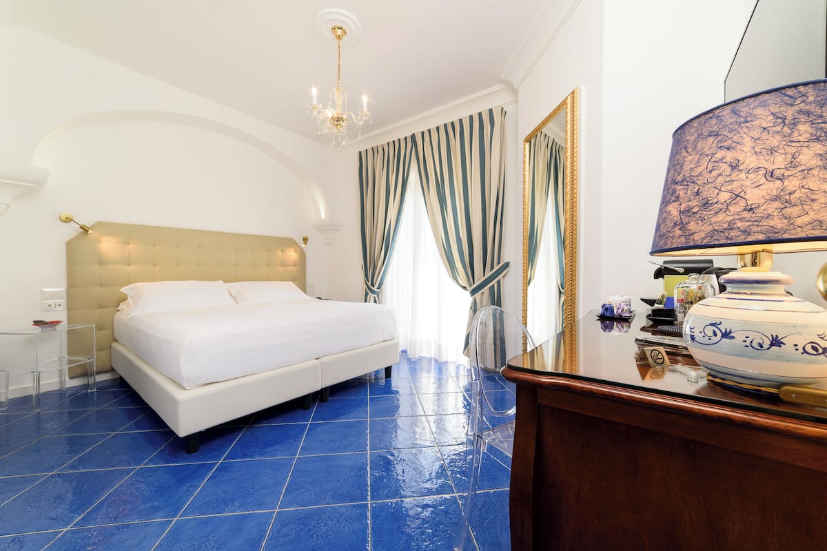 Une chambre d’hôtel avec un grand lit, un lustre, un bureau et un vase posé sur la commode.