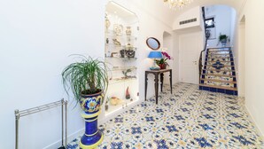 A hallway with a tiled floor, a staircase with blue and yellow tiles, a potted plant, a mirror, and a shelf with decorative items. - La Casa di Paolo Boutique Hotel (Camerota)