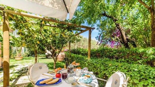 A table set for breakfast with a variety of food items and a garden view. - La Casa di Paolo Boutique Hotel (Camerota)