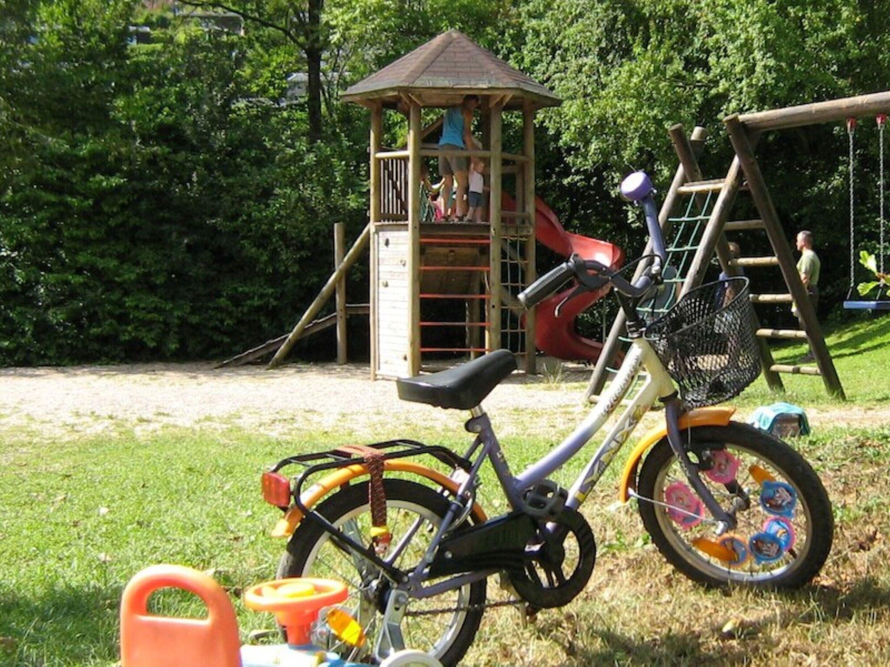 A bicycle parked in a grassy area with a playground in the background.
