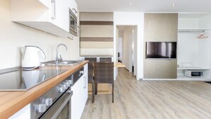 A modern kitchen with a built-in oven, a sink, and a kettle. There is a dining area with a chair and a TV mounted on the wall. - Kurzurlaub im Waxweiler-tal (Waxweiler)