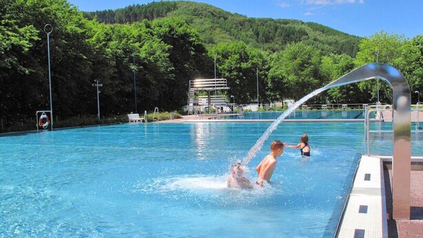 A swimming pool with a water feature, surrounded by a forested hillside. - Kurzurlaub im Waxweiler-tal (Waxweiler)