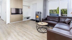 A modern living room with a sofa, a TV, a fireplace, and a view of greenery outside. - Kurzurlaub im Waxweiler-tal (Waxweiler)