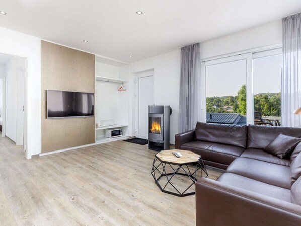 A modern living room with a sofa, a TV, a fireplace, and a view of greenery outside.