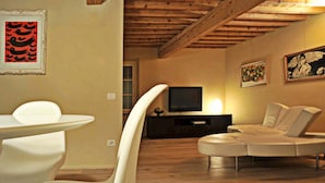 A modern living room with a wooden ceiling, a television, a sofa, and a dining area with a white table and chairs. - Apartment in Lucca Near Amphitheater Square (Lucca)